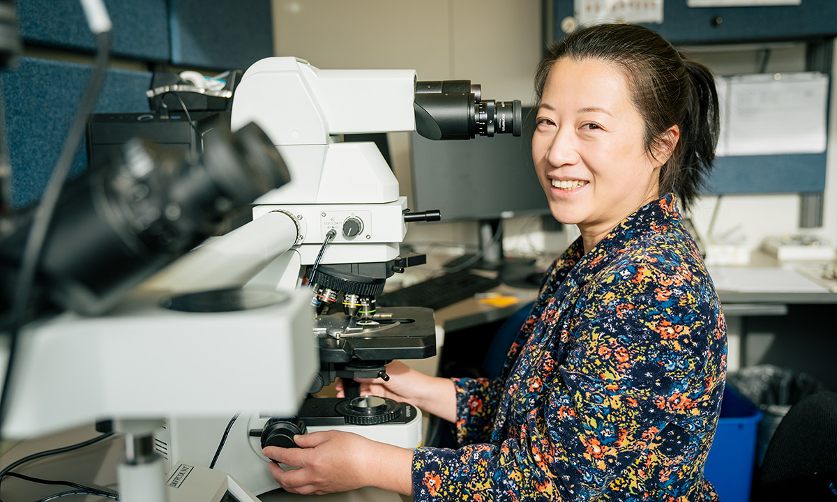 Peng Li sits in a lab in front of an electronic microscope.