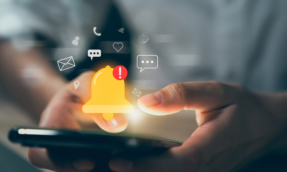 Photo illustration of a man holding a smartphone, while a notification alert with an exclamation point floats above the phone