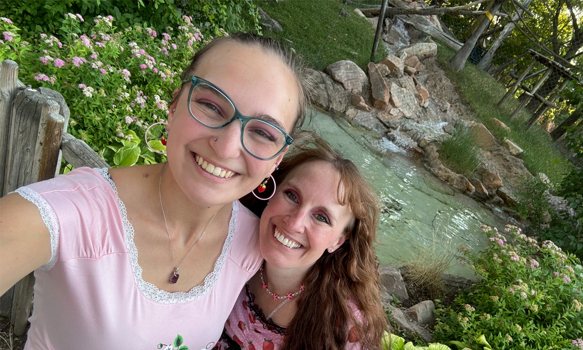 Donna Mills and Samantha Mills stand in a garden in front of a pond.