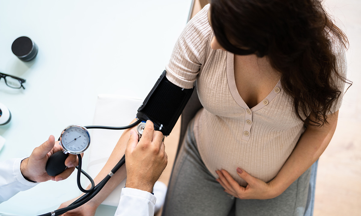 A pregnant woman sits on a chair while a clinician is checking her blood pressure.